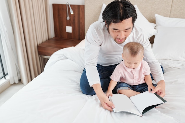 Man zit op bed met zijn zoontje en leest hem een interessant boek als hij thuis blijft vanwege een coronavirus-pandemie