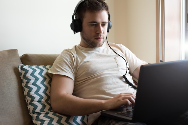 Man zit op de bank met koptelefoon en laptop