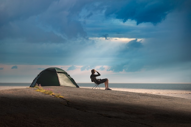 man zit op een campingstoel op een stenen eiland. Onweer nadert.