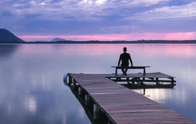 Foto man zit op een houten pierbank en kijkt naar de zonsopgang bij lagoa da conceicao florianopolis brazil