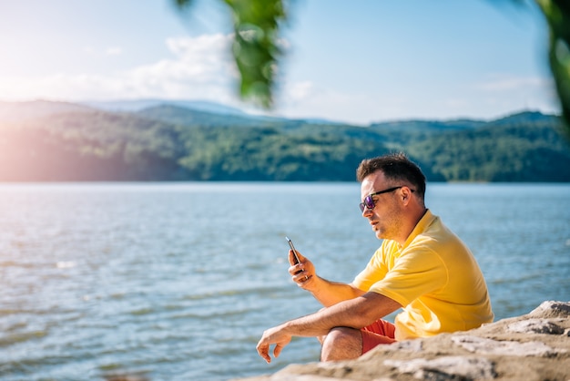 Man zittend op een strand en het gebruik van slimme telefoon