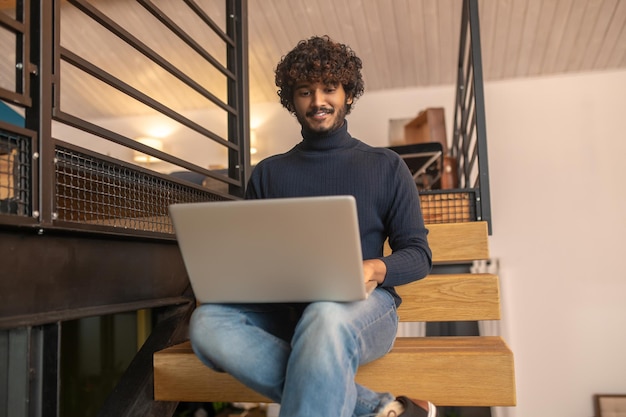 Man zittend op trappen glimlachend kijken naar laptop