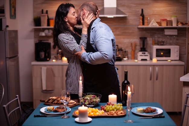 Man zoent opgetogen vrouw terwijl hij hun relatie in de keuken viert met lekker eten. Man bereidt feestelijk diner met gezond voedsel, kookt voor zijn vrouw een romantisch diner,