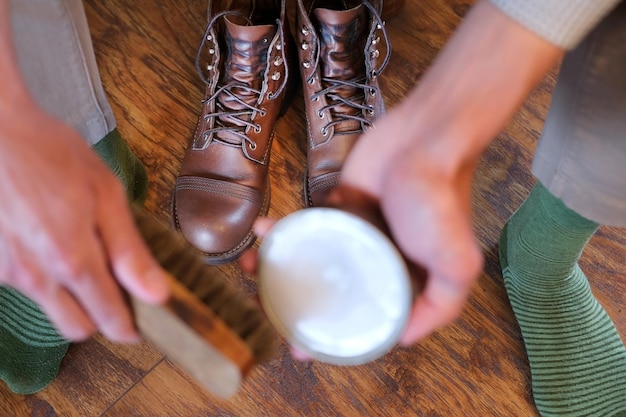 Foto man zorgt voor schoenen met een nertsolie (schoencrème) en leren mooie laarzen staan voor hem