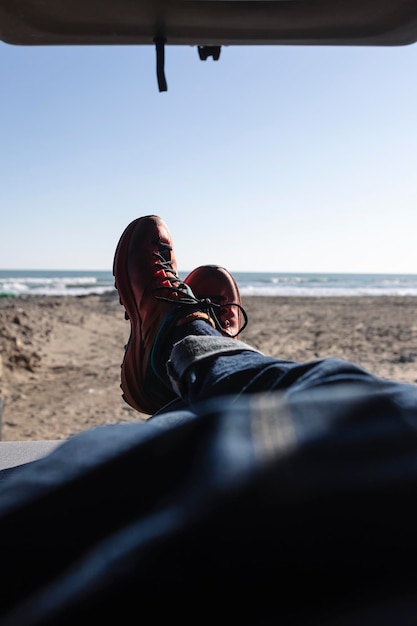 Man39s benen in spijkerbroek en wandelschoenen liggend in een busje op het strand
