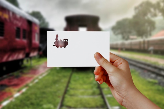 Foto la mano dell'uomo che tiene la carta simbolo del treno sulla stazione ferroviaria concetto di viaggio sogno libertà la mano tiene il treno di carta contro la ferrovia con spazio vuoto per il testo