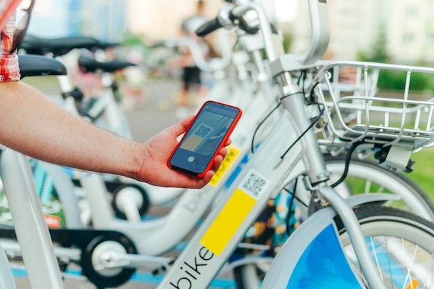 Man39s hand met een smartphone scant de qr-code op een fiets een man neemt een deelauto op straat fietsverhuur op straat via mobiele applicatie achtergrond