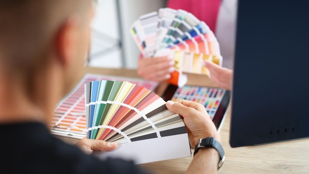 manager and client holding color swatch cards while sitting at table in design studio client