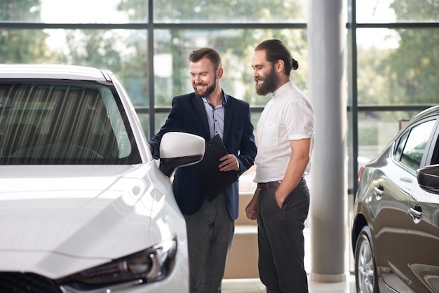 Manager die aan klant van de witte auto van het autocentrum toont.