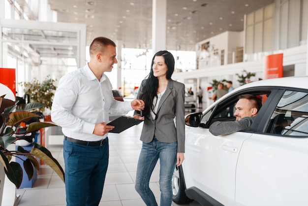 Manager en gelukkig paar dichtbij de nieuwe auto in showroom.