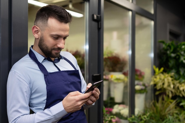 Manager in a flower shop with a phone in his hands next to a refrigerator with bouquets