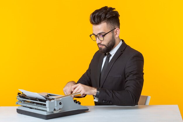 Manager in formal suit typing text on a typewriter on a yellow wall