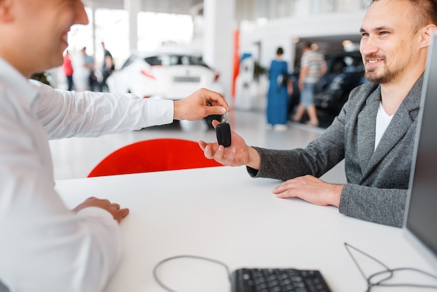 Manager gives to buyer key, new car in showroom.