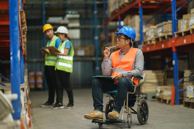 Manager handicapped in wheelchair man employee using tablet check stock work at warehouse Worker wearing high visibility clothing and hard hat helmet and checking count up goods boxes for delivery