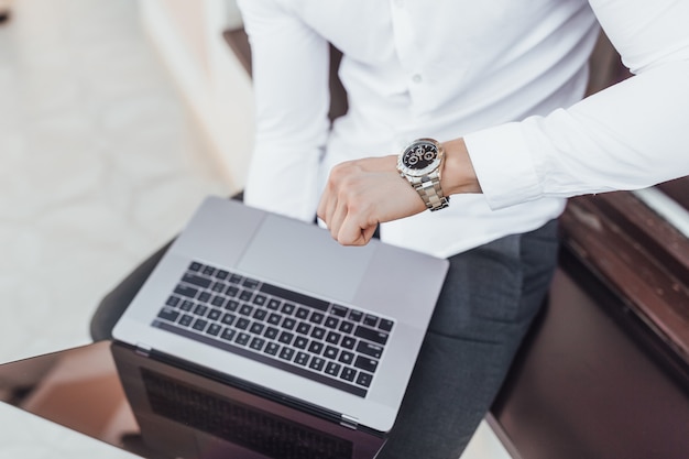 The manager holds a laptop and looks at the clock