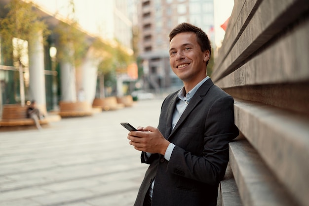 The manager is standing near the office writing a message to the client He looks away and smiles