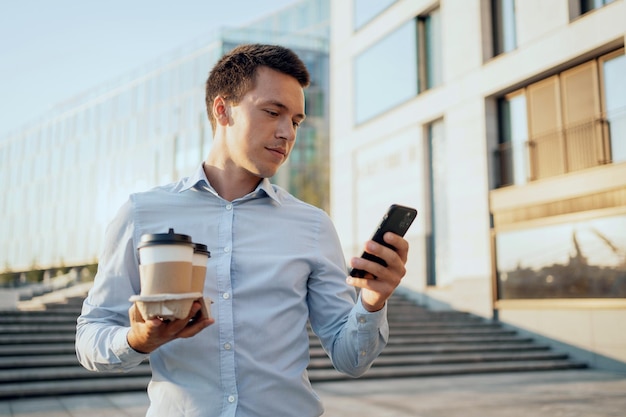 The manager is a successful stylish man holding hot coffee and a gadget in his hands