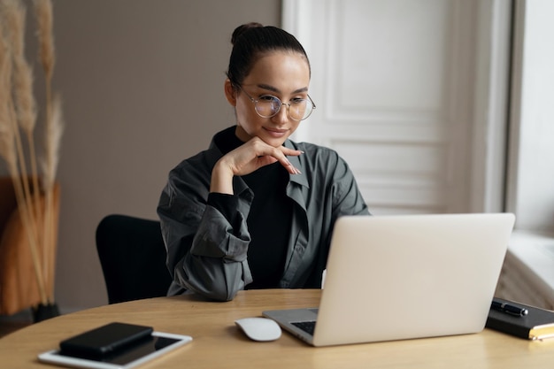 The manager is a woman with glasses working in the office using a laptop computer online