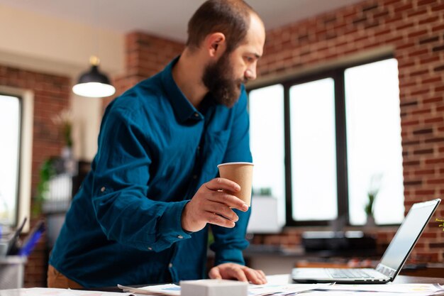 Manager che pianifica la riunione aziendale che analizza il rapporto sulla strategia di marketing sul computer che lavora alla presentazione degli investimenti nell'ufficio di avvio. uomo d'affari guardando i documenti finanziari. concetto di business