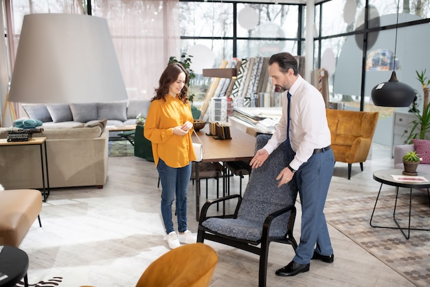 Manager in tie and white shirt showing armchair to the customer