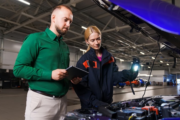 The manager together with a young female car mechanic performs diagnostics under the hood of the car Modern professional service station equipment
