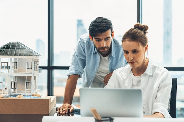 Manager werkt met behulp van laptop terwijl ingenieur huismodel Tracery inspecteert