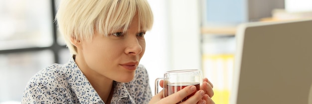 Manager with glass mug of tea looks at computer monitor in company office woman studies