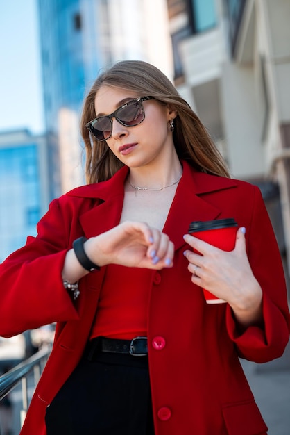 Manager woman in elegant clothes standing near windows in office on and looking at wristwatch