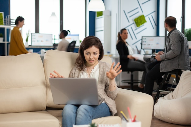 Manager woman sitting on couch holding laptop and talking on video call during