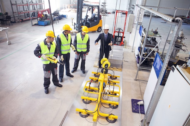 Manager and workers near metal sheet lifting device at factory