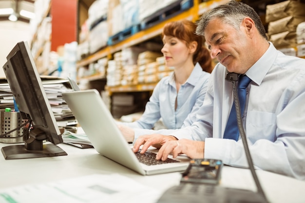 Manager working on laptop and talking on phone at desk