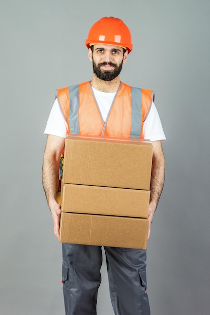 Строитель в оранжевом шлеме с картонной коробкой в руках на сером фоне