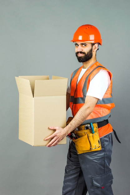 A manbuilder in an orange helmet with a cardboard box in his hands On a gray background