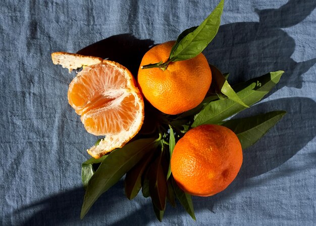 Mandarijnen of sinaasappels, clementines, citrusvruchten met groene bladeren op pastelblauwe textielachtergrond