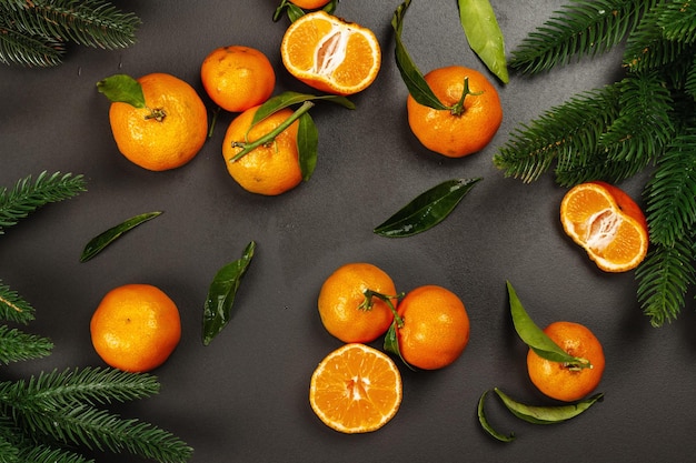 Mandarijnen (sinaasappels, mandarijnen, clementines, citrusvruchten) met bladeren en dennentakken. Zwarte stenen achtergrond, feestelijk plat, bovenaanzicht