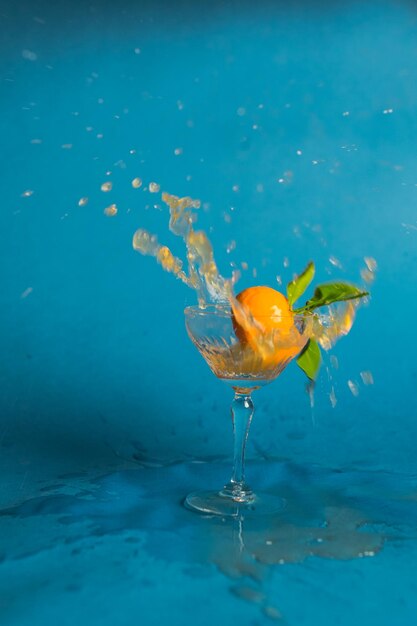 Mandarin tangerine orange dropped and splashing into cocktail glass against blue