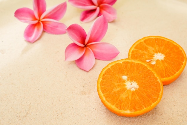 Mandarine Orange Cut in Half On Sand With Plumeria Flowers