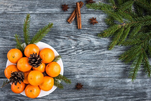 Mandarines on wooden with Christmas fir branches, cinnamon sticks, anise stars and cones.