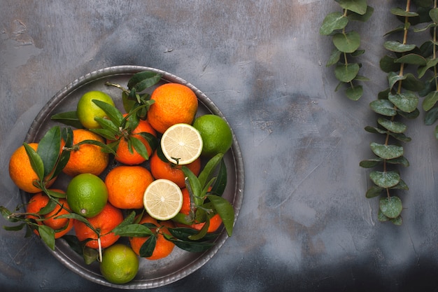 mandarins with green leaves on a metal plate, on a gray background