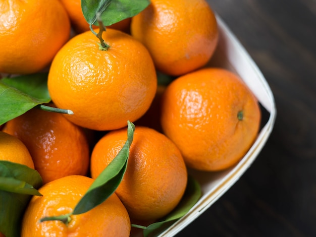 Mandarins with leaves in a wooden box on a wooden black background, top view