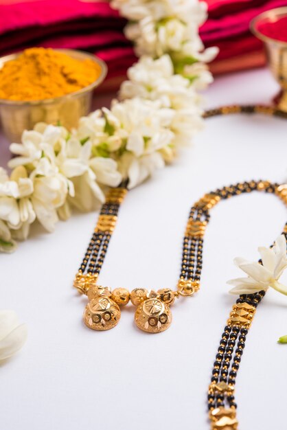 Photo mangalsutra or golden necklace to worn by a married hindu women, arranged with traditional saree  with huldi kumkum and mogra flowers gajra, selective focus
