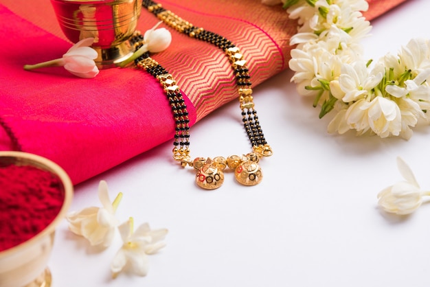 Photo mangalsutra or golden necklace to worn by a married hindu women, arranged with traditional saree  with huldi kumkum and mogra flowers gajra, selective focus