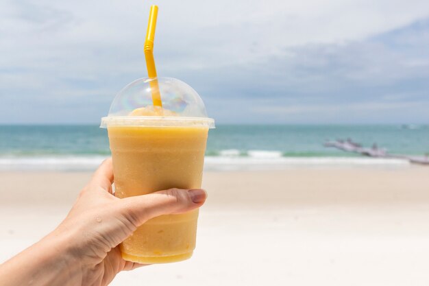 Mango ananas verse koude smoothie in de hand tegen zeegezicht