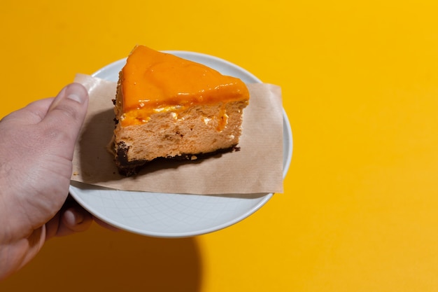 Mango cheesecake slice with sea buckthorn topping in male hand on an orange seamless background