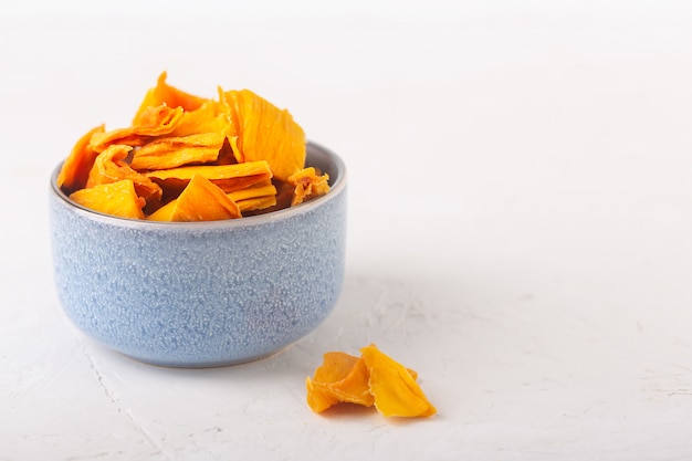 Chip di mango in una ciotola blu e pezzi di questo frutto su un tavolo