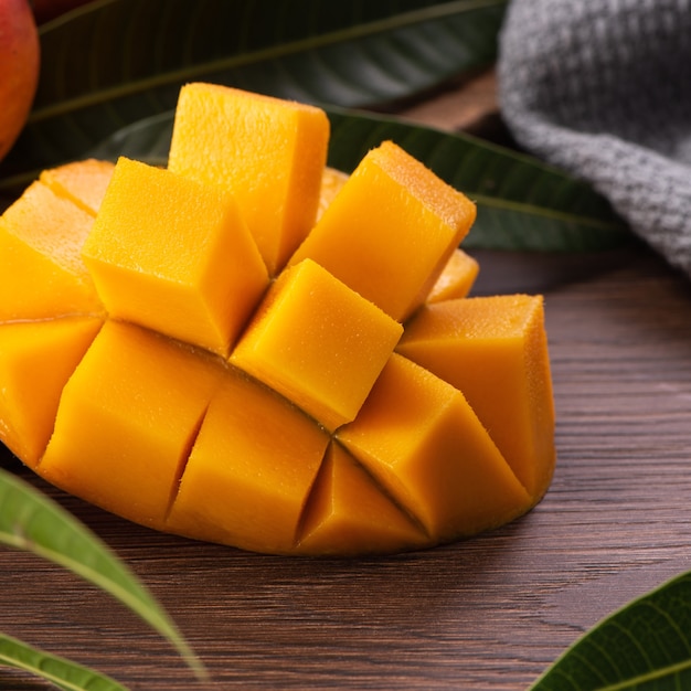 Mango. Close up of fresh ripe mango fruit with leaves over dark wooden table background with green leaves.