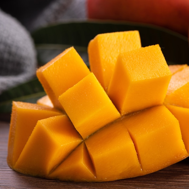 mango. close up of fresh ripe mango fruit with leaves over dark wooden table background with green leaves.