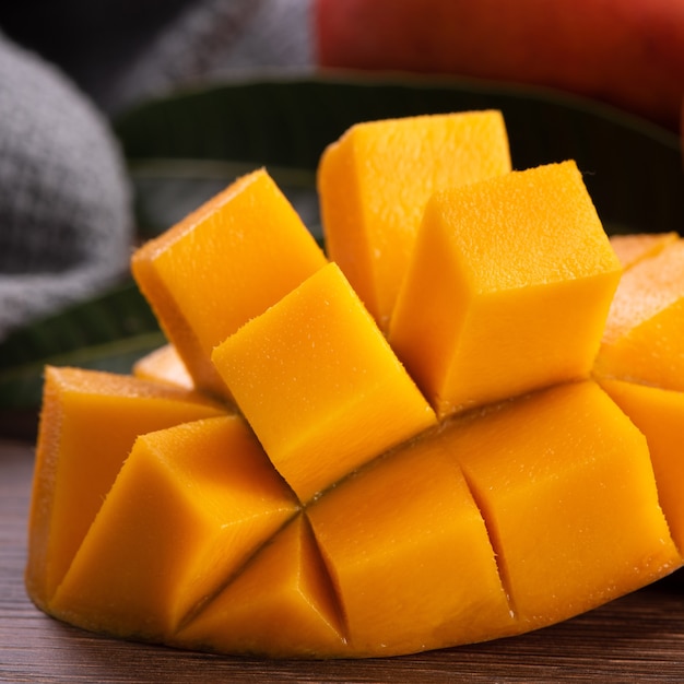 Mango. Close up of fresh ripe mango fruit with leaves over dark wooden table background with green leaves.