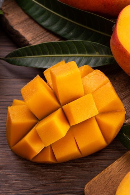 Mango. Close up of fresh ripe mango fruit with leaves over dark wooden table background with green leaves.