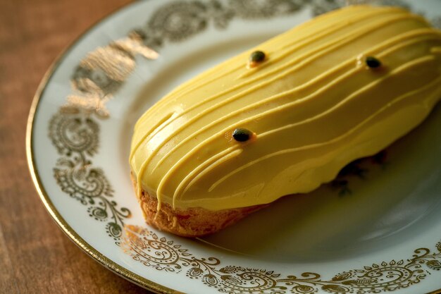 Mango-eclair met geel glazuur in witte plaat op houten ondergrond